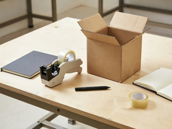 A notebook, tape gun and marker on a packing bench beside a test carton
